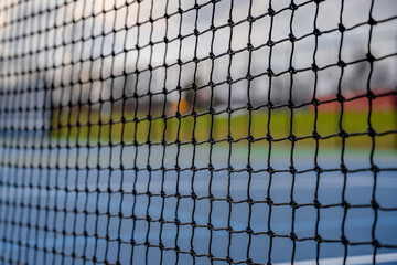 Close-up photo of a tennis court net set against a blue tennis court