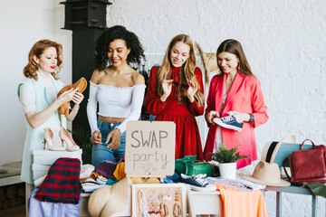 four young woman female caucasian and african students at swap party try on clothes, bags, shoes and accessories, change clothes with each other, second hand for things, zero waste life, eco-friendly