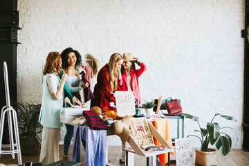 four young woman female caucasian and african students at swap party try on clothes, bags, shoes and accessories, change clothes with each other, second hand for things, zero waste life, eco-friendly