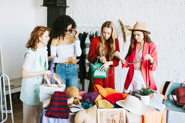 four young woman female caucasian and african students at swap party try on clothes, bags, shoes...