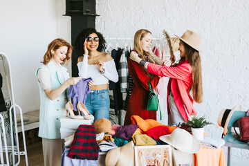 four young woman female caucasian and african students at swap party try on clothes, bags, shoes...