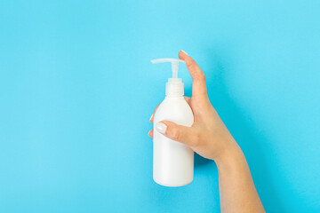 Housewife's hand holds a spray with cleaning agent on a blue background. Detergent for various surfaces in the kitchen, bathroom and other rooms. Close-up. Light pastel blue background. place for text