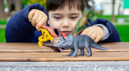 cute kid is playing with  dinosaurs toys on park bench, spring, green nature, grass. happy dinosaur day, may 15 and june 1. fascinating dinosaur fantasies. spring outside, public park,having fun. © Alexandra