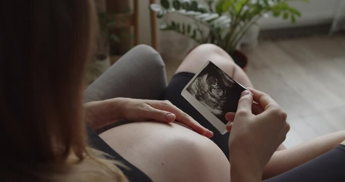 Relaxing pregnant woman holds ultrasound picture of her baby. The expectant loving mother caresses her baby in the tummy. Belly of a pregnant woman. Maternity prenatal care and pregnancy concept.