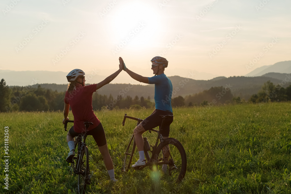 Wall mural road cyclists, man and woman, stopping at a grassy hill to celebrate the race achievement with high 