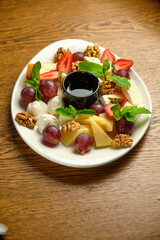 A plate with several varieties of cheese and fruit. Jam sauce in the middle of the plate