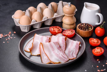 Delicious fresh raw bacon cut with slices on a grey plate against a dark concrete background
