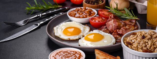A delicious nutritious healthy breakfast with fried eggs, bacon, beans, a glass of juice, oat cookies, milk and jam