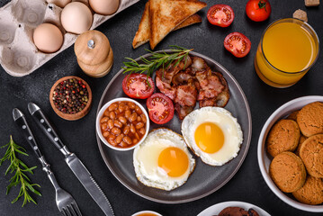 A delicious nutritious healthy breakfast with fried eggs, bacon, beans, a glass of juice, oat cookies, milk and jam