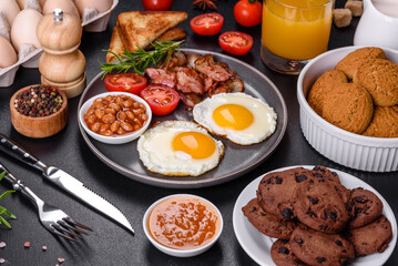 A delicious nutritious healthy breakfast with fried eggs, bacon, beans, a glass of juice, oat cookies, milk and jam