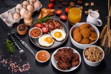 A delicious nutritious healthy breakfast with fried eggs, bacon, beans, a glass of juice, oat cookies, milk and jam