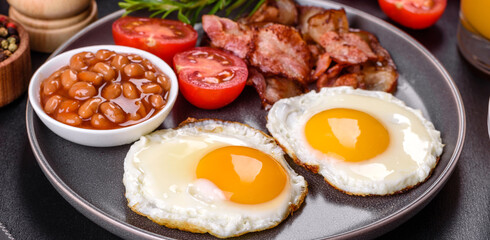 A delicious nutritious healthy breakfast with fried eggs, bacon, beans, a glass of juice, oat cookies, milk and jam
