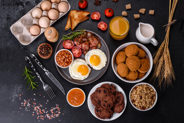A delicious nutritious healthy breakfast with fried eggs, bacon, beans, a glass of juice, oat cookies, milk and jam