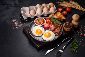 A delicious nutritious healthy breakfast with fried eggs, bacon, beans, a glass of juice, oat cookies, milk and jam