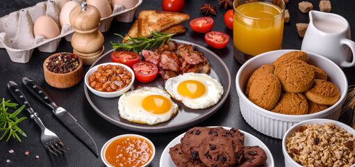 A delicious nutritious healthy breakfast with fried eggs, bacon, beans, a glass of juice, oat cookies, milk and jam
