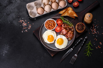 A delicious nutritious healthy breakfast with fried eggs, bacon, beans, a glass of juice, oat cookies, milk and jam