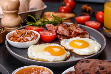A delicious nutritious healthy breakfast with fried eggs, bacon, beans, a glass of juice, oat cookies, milk and jam