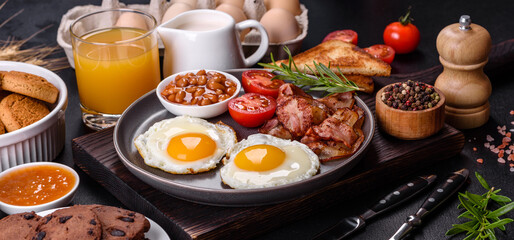 A delicious nutritious healthy breakfast with fried eggs, bacon, beans, a glass of juice, oat cookies, milk and jam