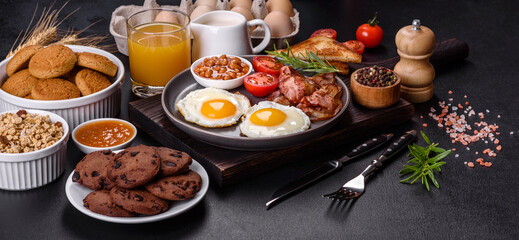 A delicious nutritious healthy breakfast with fried eggs, bacon, beans, a glass of juice, oat cookies, milk and jam