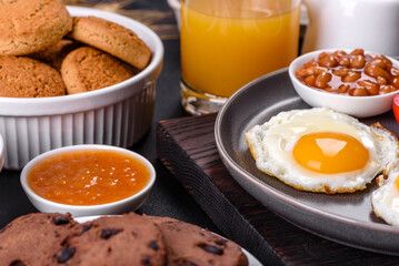 A delicious nutritious healthy breakfast with fried eggs, bacon, beans, a glass of juice, oat cookies, milk and jam