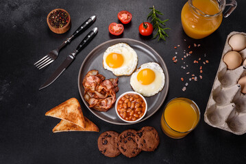 A delicious nutritious healthy breakfast with fried eggs, bacon, beans, a glass of juice, oat cookies, milk and jam