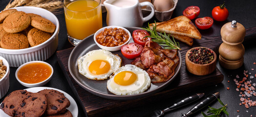 A delicious nutritious healthy breakfast with fried eggs, bacon, beans, a glass of juice, oat cookies, milk and jam