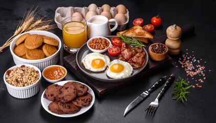 Fototapeta na wymiar A delicious nutritious healthy breakfast with fried eggs, bacon, beans, a glass of juice, oat cookies, milk and jam