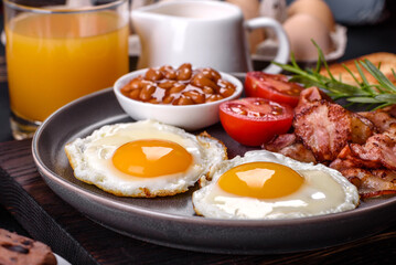 A delicious nutritious healthy breakfast with fried eggs, bacon, beans, a glass of juice, oat cookies, milk and jam