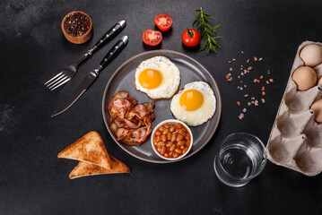 A delicious nutritious healthy breakfast with fried eggs, bacon, beans, a glass of juice, oat cookies, milk and jam