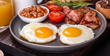 A delicious nutritious healthy breakfast with fried eggs, bacon, beans, a glass of juice, oat cookies, milk and jam