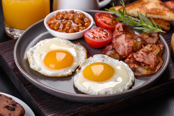 A delicious nutritious healthy breakfast with fried eggs, bacon, beans, a glass of juice, oat cookies, milk and jam