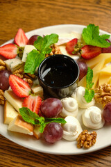 A plate with several varieties of cheese and fruit. Jam sauce in the middle of the plate