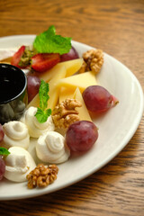 A plate with several varieties of cheese and fruit. Jam sauce in the middle of the plate