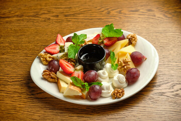 A plate with several varieties of cheese and fruit. Jam sauce in the middle of the plate