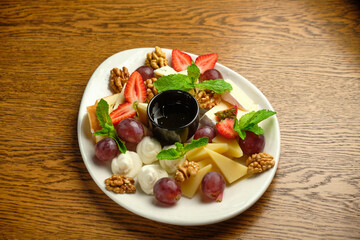 A plate with several varieties of cheese and fruit. Jam sauce in the middle of the plate