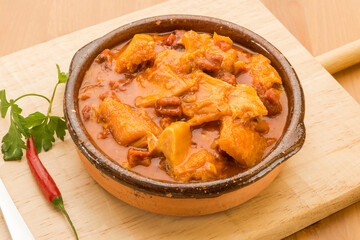 Typical Spanish food, stewed tripe a la madrilena. 
Horizontal view of food in a clay pot on a wooden table.