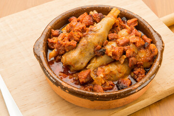 Typical Spanish food, lamb trotters with ham and chorizo. Horizontal view of food in a clay pot on a wooden table.