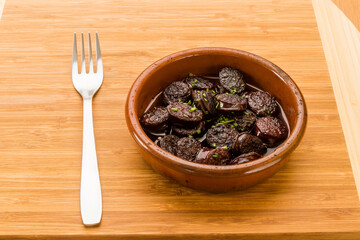 Typical Spanish food, portion of chorizo ​​in wine. 
Horizontal view of food in a clay pot.