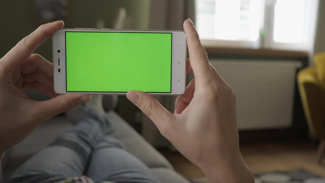 Phone With Green Mock-up Screen Chroma Key Surfing Internet Watching Content Videos Blogs Tapping on Center Screen. Point of View of Woman at Living Room Sitting on Chair Using Phone With Green Mock-u