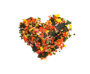 Fototapeta na wymiar Dry multi-colored compound fishfeed flakes in the shape of a heart on White background. .