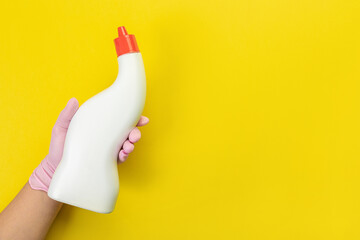 Close up of female hand in pink gloves holds  bottle with cleaner liquid for washing dishes with place for text on yellow background. Cleaning supplies concept. Copy space for ad.