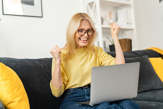 Overjoyed happy middle aged 60s mature woman in eyeglasses looking at laptop screen, reading email with amazing news, celebrating online lottery win, getting bank loan approval or money refund