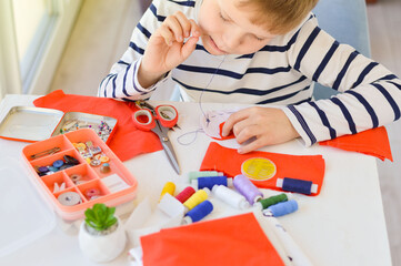 Close-up of a beautiful 9-year-old Caucasian boy who studies with a needle and thread.