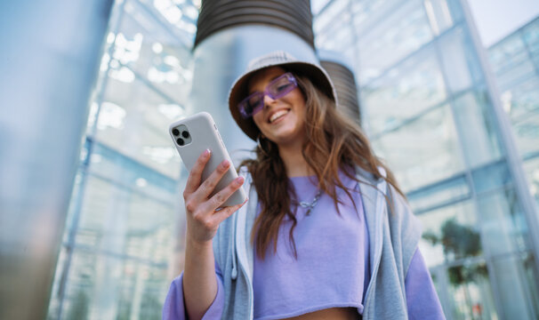 Young cool girl holding and using mobile phone. Smiling woman texting with friends