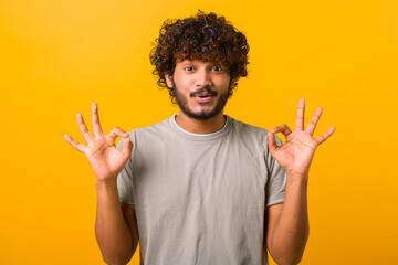 Everything is fine. Satisfied bearded curly Indian man showing ok gesture with fingers, approving work, satisfied with quality. Indoor studio shot isolated on yellow background - obrazy, fototapety, plakaty