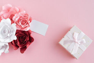 Paper roses with blank card and gift box with ribbon on pink background. Copy space. Mother's Day. Greeting card.