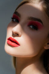 Fototapeta premium Young woman with red visage standing in shadow isolated on grey.