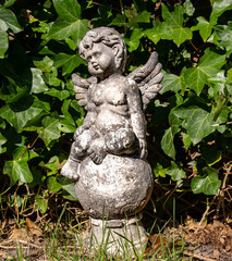 An old, damaged statue of an angel on a background of ivy leaves