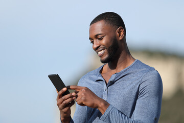 Happy man with black skin using smart phone outside