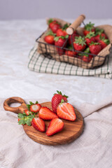 Erdbeeren im Drahtkorb auf einem Tisch mit Holzbrett und geschnittenen Erdbeeren